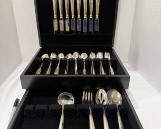 Flatware Set in Black Storage Chest with Gold-Tone Accents A flatware set stored in a black lined chest with a pull-out drawer, including eight knives, forks, spoons and serving pieces such as a ladle, a slotted spoon and a serving fork. The handles have gold-tone accent bands. A ready-to-store flatware set for dinner parties.