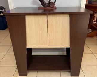 Two-Tone Storage Cabinet with Twisted Root Sculpture A two-tone cabinet with light woodgrain doors, a dark espresso-tone frame and an open lower shelf, shown with a twisted root-style sculpture on a wood base. A modern storage console for a living room or entry. Confirm whether the sculpture is included.