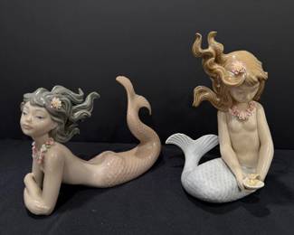 Lladró Porcelain Mermaid Figurines – Pair Two Lladró porcelain mermaid figurines: one lying stretched out with her tail raised, and one seated holding a shell with a pearl. Both have flowing sculpted hair and porcelain flower accents. A sweet pair for Lladro mermaid collectors or a coastal-themed shelf.