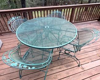 Metal Mesh Patio Dining Set with Four Chairs A teal-green metal patio set with a round mesh-top table with an umbrella hole and four curved-back mesh chairs with leaf and flower scroll details. A classic outdoor dining set for a deck or garden. The paint shows light outdoor wear.