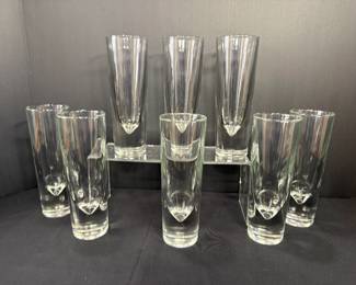 Set of Eight Tall Teardrop-Bottom Glasses with Acrylic Riser Eight tall clear glasses with heavy bases and a sculpted teardrop shape inside each bottom, shown on and around an acrylic display riser. Modern highball glasses for cocktails, iced tea or sparkling water.