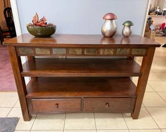 Wood Console Table with Slate Tile Inlay and Two Drawers A wood console table with a band of slate-look tile inlay below the top, two open shelves and two drawers with round knobs. This sofa table or entry table offers both display and storage space. Decor shown may not be included.