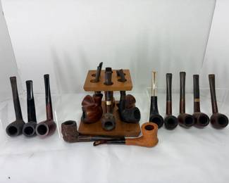 Estate Tobacco Pipe Collection with Wooden Pipe Stand About sixteen tobacco pipes with smooth and rusticated bowls in straight and bent shapes, plus a wooden pipe stand. A strong lot for pipe collectors and smokers. Makers' stamps are not visible in the photo.
