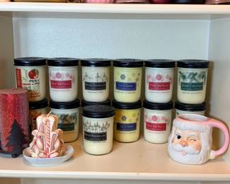 Swan Creek Candle Co. Holiday Jar Candles and Santa Mug A shelf of Swan Creek Candle Co. jar candles in holiday scents such as Winter Wonderland, Let It Snow, Deck the Halls and Merry Christmas, plus a red glitter pillar candle, a carved candy cane-style candle and a winking Santa mug. A festive Christmas candle lot.