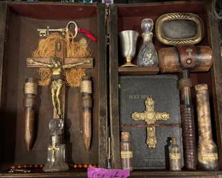 Artisanal Vampire Hunting Kit Casket Curio (One-of-a-Kind) Covers the intricate velvet-lined wooden chest containing the stakes, crucifix, holy water, and bible. A spectacular centerpiece for any high-end oddities collection. This bespoke, one-of-a-kind Vampire Hunting Kit is masterfully curated inside a distressed, dual-tiered hardwood travel case lined in deep crimson velvet. The upper tier houses two hand-carved, twine-wrapped wooden stakes alongside an ornate brass-and-wood crucifix configuration and a vintage iron skeleton key setup. The lower compartment features an antique Holy Bible with a prominent gilded cross embellishment, accompanied by essential glass apothecary vials, a heavy ceremonial pouring chalice, and a hand-turned wooden mallet with leather bracing. A magnificent theatrical display piece that commands instant attention.