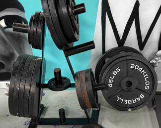 Heavy-Duty Olympic Plate Tree with Cast-Iron Weight Plates (~350 lbs.-400 lbs. total): Robust, multi-tier A-frame Olympic plate tree fully loaded with standard 2-inch Olympic cast-iron weight plates. Includes premium brands like CAP Barbell plates) and comes equipped with a padded squat neck pad on the guided barbell. The finish shows standard gym environment wear but looks structurally sound with clean guide rods.
