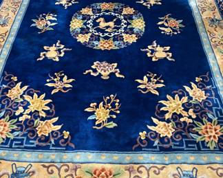 Magnificent Chinese Art Deco Sculpted Indigo Wool Rug A vibrant design statement. This stunning Vintage Chinese Art Deco Rugfeatures an ultra-thick, hand-carved, and sculpted wool pile that feels like velvet underfoot. The electric sapphire blue field is beautifully accented with traditional asymmetrical motifs of blooming lotuses, antique vases, and an elegant central mythological creature emblem. A highly collectible piece that serves as an incredible anchor for Hollywood Regency, Maximalist, or high-end eclectic interiors.
