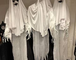 Distressed Haunting Specters / Ghost Trio Lifesize Display three life-sized white robed phantoms with blacked-out facial configurations. Bring an atmosphere of absolute dread with this trio of life-sized Haunting Specters. These professional-grade figures feature stylized, distressed white robes layered over flowing, tattered cheesecloth shrouds that catch air currents for an eerie floating illusion. Each phantom is finished with a terrifying, hollowed-out black facial facade and detailed skeletal hands reaching forward, making them an incredible high-impact visual anchor for a grand entryway or dark corridor.