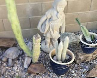 A Concrete Statue of a Little Girl Standing and Two Potted Cactus Plants