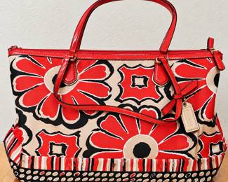 Coach Floral Print Tote Handbag ◆ Bold red, black, and cream floral design ◆ Glossy red trim and double handles ◆ Gold-tone hardware ◆ Top zipper closure ◆ Striped and dotted accents ◆ Coach hanging tag