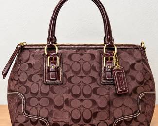 Coach Signature Jacquard Satchel Handbag ◆ Chocolate brown signature “C” pattern ◆ Dark brown leather trim ◆ Double handles ◆ Gold-tone hardware ◆ Top zipper closure ◆ Decorative buckles ◆ Contrast stitching ◆ Coach hanging tag