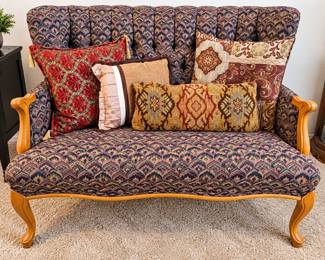 Vintage Upholstered Loveseat — High channel-tufted back, multicolored patterned fabric, curved wooden arms, and carved cabriole legs.  Assorted Decorative Throw Pillows — Coordinating brocade, floral, ruffled, and Southwestern geometric designs in rich earth tones.