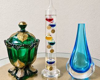 Emerald Green Decorative Glass Jar ◆ Rich green glass ◆ Ornate gold-tone embellishments ◆ Scalloped rim ◆ Matching decorative lid ◆ Footed base  Galileo Glass Thermometer ◆ Tall clear glass cylinder ◆ Colorful floating glass bulbs ◆ Gold-tone temperature tags ◆ Decorative scientific instrument  Blue Art Glass Vase ◆ Aqua and cobalt blue tones ◆ Teardrop shape ◆ Clear glass base ◆ Sculptural design ◆ Narrow opening