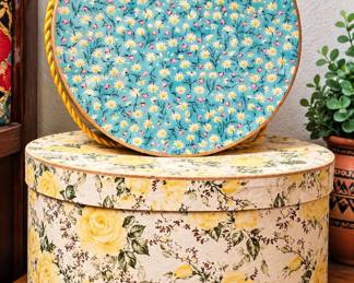 Two decorative round floral storage boxes featuring turquoise daisies and vintage yellow rose patterns.