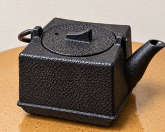 Square Black Cast-Iron Teapot — Japanese-style geometric design with textured finish, round fitted lid, angular knob, and curved pouring spout.