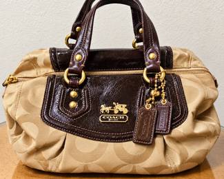 Coach Signature Jacquard Satchel Handbag ◆ Beige signature “C” pattern ◆ Dark brown patent leather trim ◆ Double handles ◆ Gold-tone hardware ◆ Top zipper closure ◆ Coach logo plaque and hanging leather tags