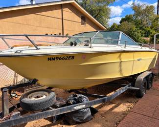 Vintage yellow fiberglass motorboat with windshield, stainless steel railings, and tandem-axle trailer. Condition and mechanical operation unknown.
