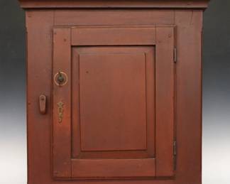 A 19th century American painted hanging cupboard.  Poplar construction features a molded top over a single paneled door with rotating catch on a molded base with old Red painted finish.  Painted "1828" and "1878" numerals at back.  Older painted finish with minor wear and scuffs, shrinkage.  27 1/2 x 12 x 30" high overall.  