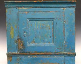 A mid 19th century European painted hanging corner cupboard.  Pine construction features applied moldings surrounding a paneled door with shelved interior and lower drawer.  Old Blue painted finish with wear, shrinkage and minor damage, lacks lock.  Requires a 26 1/2" corner, 25 3/4" high overall.  