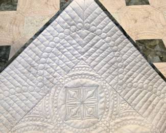 Close-up of the quilt’s finished corner and reverse: straight-line quilting, pebble-like circles, intricate geometric motifs, and neatly finished contrasting binding.