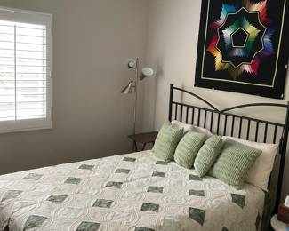 Finished cream-and-sage quilt displayed on a bed, revealing its complete arrangement of green diamonds, circular quilting, and coordinating border.