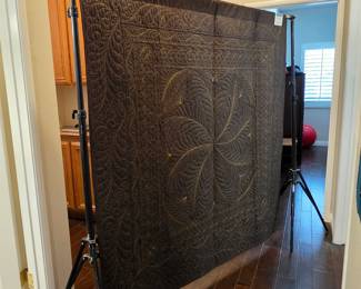 The quilt’s reverse reveals an elaborate stitched composition: a central feathered rosette, sweeping scrolls, and richly quilted borders rendered in contrasting thread on dark fabric.