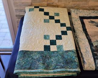 Cream and teal chain patchwork quilt with diagonal square motifs, a broad patterned border, and elaborate feather quilting visible across the light background.