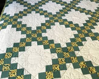 Close-up of the chain patchwork quilt: green squares and golden sunflower-print fabrics surround cream areas with circular and geometric stitching.