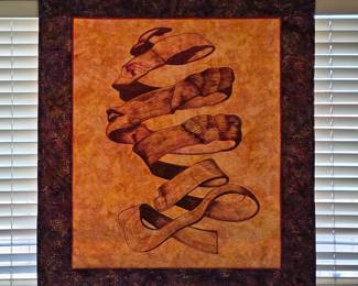Ballet-themed quilted wall hanging featuring pointe shoes and flowing ribbons against a warm golden background, framed by a deep, richly patterned border.