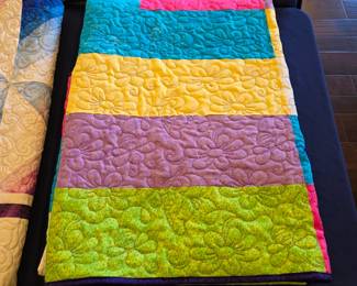 Bright patchwork quilt in turquoise, lime, lavender, yellow, and pink. Rounded floral quilting adds another layer of pattern and texture to the bold fabric blocks.