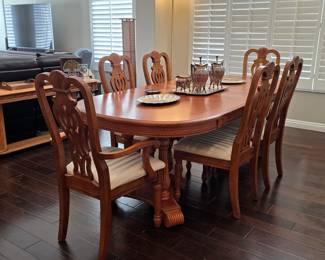 Traditional oak dining set including an oval pedestal dining table and six carved high-back chairs with striped fabric seat cushions.