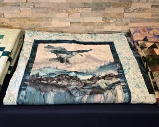 Eagle-themed wildlife quilt with a scenic mountain panel, layered fabric borders, and decorative machine quilting in a cool palette of blue, gray, and cream.