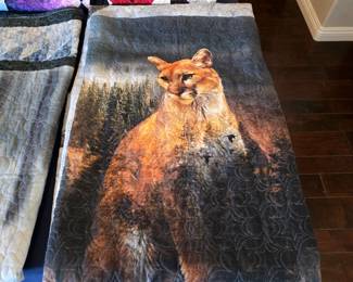 Mountain lion quilt featuring a dramatic woodland wildlife panel and intricate flowing quilting across the animal and forest background. Rich gold, charcoal, and evergreen tones.