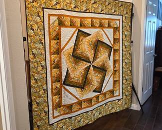 The "Farris Wheel" - Intricately pieced medallion quilt in gold, olive, cream, and brown. Angular shapes create a twisting central design surrounded by layered borders and floral fabrics.