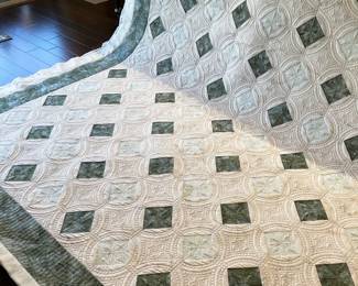 Close view during quilting: small green diamonds surrounded by densely stitched circles and geometric motifs. The changing stitch density creates pronounced texture across the cream background.