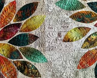 Detail between the appliqué blossoms reveals intricate pebble and scroll quilting, sweeping feather motifs, and individually quilted petals against a text-print fabric background.