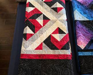 Red, black, and cream patchwork quilt with angular piecing, intersecting light bands, and elaborate scroll quilting extending into the broad black border.