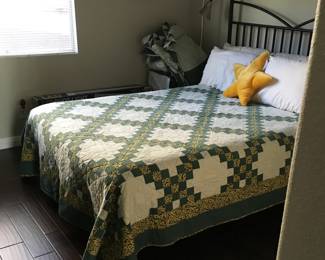 Green-and-gold chain patchwork quilt displayed on a bed. Diagonal lines of small squares frame cream sections filled with decorative quilting.