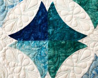Blue, teal, and white curved patchwork with custom quilting fitted to the shapes. Feather motifs fill the white sections, while decorative stitching enriches the colored fabrics.