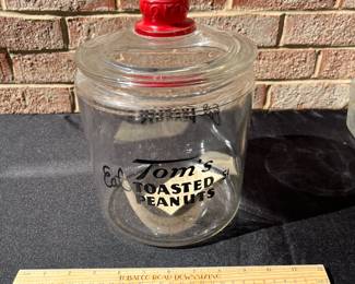A80 - $55. Tom’s Toasted Peanuts Glass Jar. Measures 10 inches tall. It has some small scratches on the inner rim of the glass.