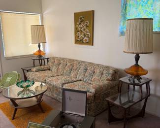 Charming 1960s living room featuring a vintage floral sofa, mid-century lamps, retro coffee table, record player, and nostalgic home décor.