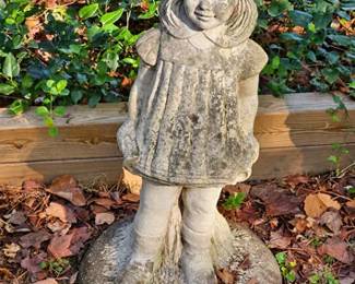 Concrete garden statue of a young girl wearing a pleated dress