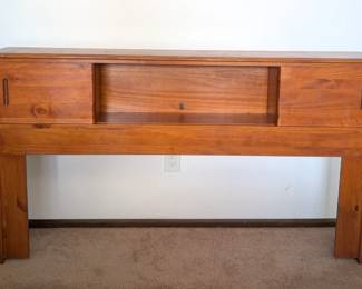 Headboard with sliding storage compartments. Full size bed fits into the opening and queen size sits up against it comfortably.