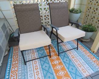 Two folding patio chairs with cushioned seats and outdoor area rug.