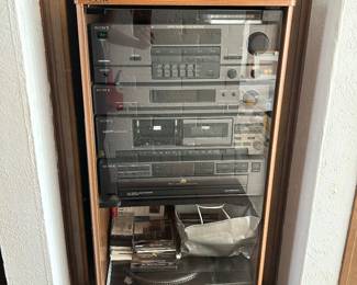 Stacked stereo components in a wood cabinet, with audio accessories below.
