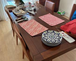 Wood dining table and chairs with placemats and assorted tabletop items.