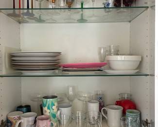 Assorted cups, mugs, plates, and bowls in a kitchen cabinet.