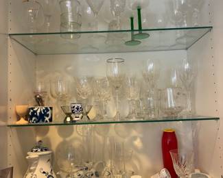 Clear glass stemware, drinking glasses, and decorative glass pieces in a display cabinet.