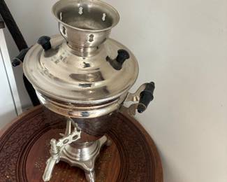 Metal samovar-style tea urn on a round carved wooden table.