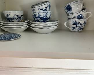 Blue-and-white patterned teacups and saucers in a cabinet.
